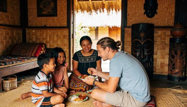 Sharing meal with local family in thatched bamboo hut featuring warm cultural exchange