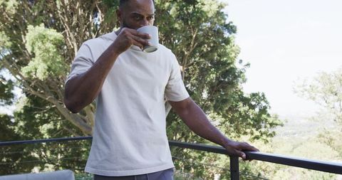 Mature african man sipping coffee on balcony overlooking green valley and trees
