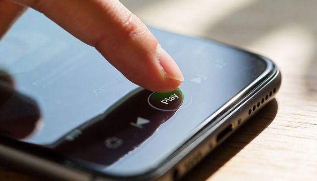 Fingertip Pressing Play Button on Smartphone Touchscreen Macro Closeup for Media