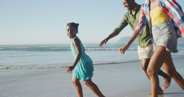 Happy african american couple running with daughter on sunny beach. healthy and active time beach holiday.