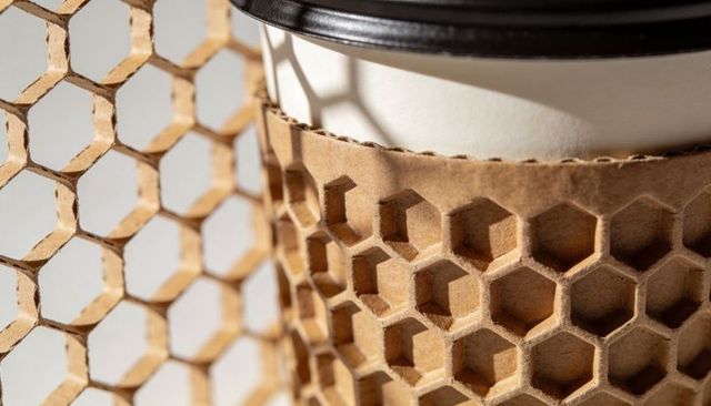Kraft honeycomb coffee sleeve casting geometric shadows on paper coffee cup with black lid
