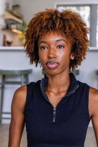 Confident african american woman posing in modern kitchen wearing black ribbed zip-front top