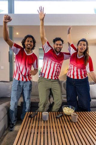 Indian friends cheering in red-white jerseys watching live match in modern living room