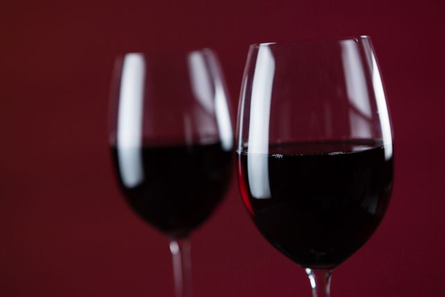 This image features two wine glasses filled with red wine against a deep red background. Ideal for use in advertisements for wine brands, restaurant promotions, romantic event invitations, or articles about wine tasting and gourmet dining.