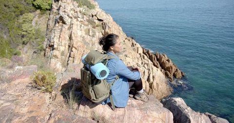 Woman hiking with backpack and yoga mat on scenic cliff edge