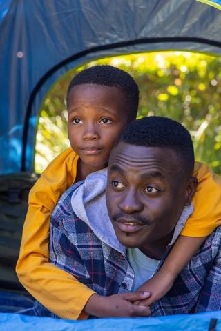 African american father giving piggyback to son inside tent on camping trip