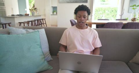 African american man working remotely on laptop wearing headphones sitting on modern sofa