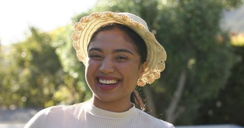 Sunlit smiling woman wearing straw hat enjoying warm outdoor moment with bokeh greenery