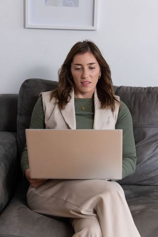 Adult woman working from home on laptop on modern neutral sofa