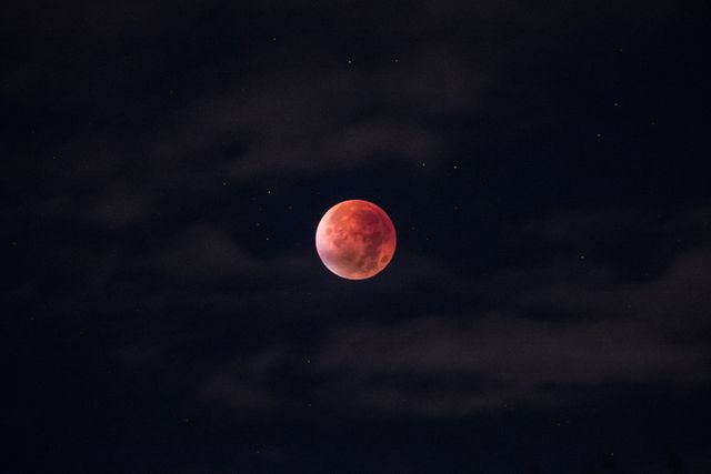 Blood moon during a lunar eclipse contrasts starkly against dark night sky with scattered stars. Perfect for educational content about astronomy, celestial events, lunar phenomena, or as a striking visual for space-themed projects or backgrounds.