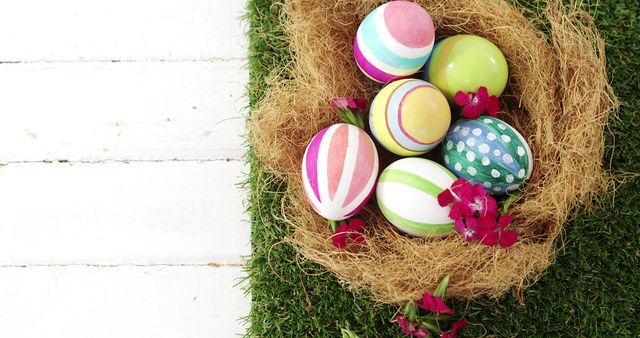 Colorful painted Easter eggs are nestled in a nest with vibrant flowers on a grassy surface, with copy space. These eggs symbolize the joy and renewal of the Easter holiday.