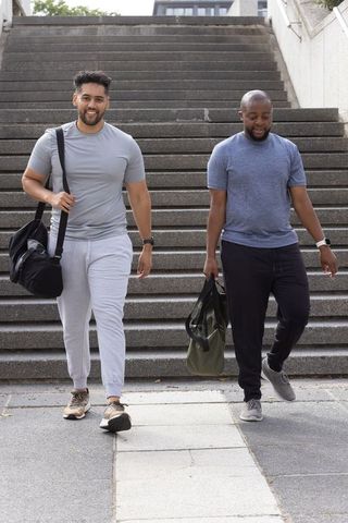Asian and african american men walking down stairs carrying gym bags in urban plaza