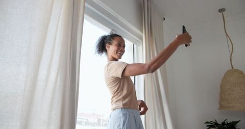 African American Woman Taking Selfie by Sunlit Window in Cozy Room