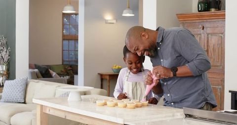 Father and Daughter Decorating Cupcakes Together in Kitchen