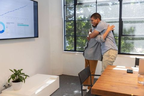 Coworkers Celebrating Success with Hug in Office Room