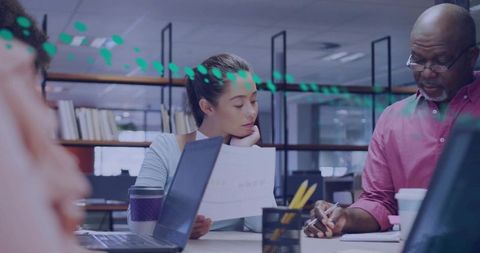 Team reviewing printed report and collaborating around laptops in open office workspace