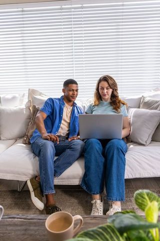 Interracial couple using laptop on cozy cream sofa planning together
