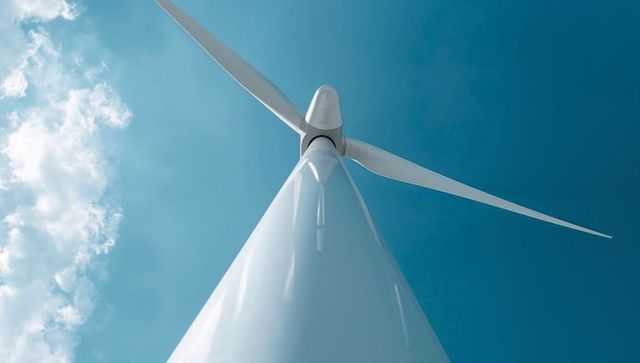 Towering wind turbine reaching skyward with three blades against clear blue sky