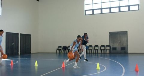 Female basketball players practicing dribbling with coach inside gym