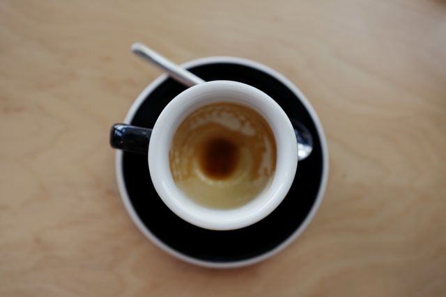 Top-down view of an empty espresso cup on wooden table, with black saucer and spoon. Ideal for use in food blogs, coffee shop promotions, product advertisements, and minimalistic design elements.