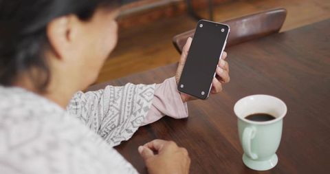 Senior Woman Holding Smartphone at Home Near Coffee Mug