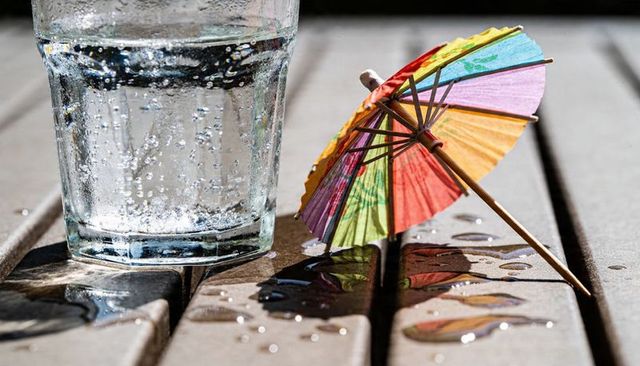 Sparkling glass catching sunlight beside colorful paper umbrella on slatted table