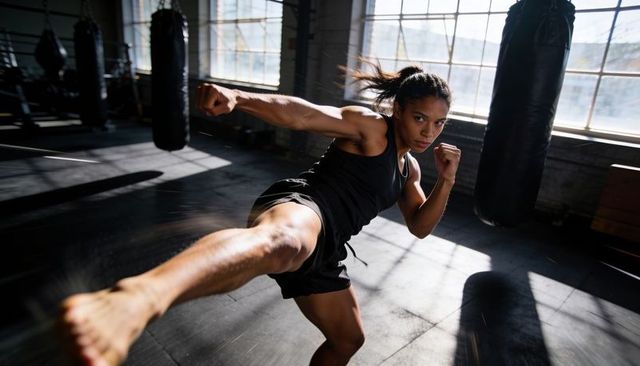 Female athlete launching powerful high kick in sunlit gym with motion blur and intensity