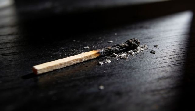 Burnt matchstick on dark wood surface with charred head and ash detail