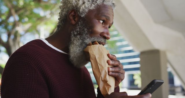 Elderly Man Enjoying Snack While Checking Phone Outdoors - Download Free Stock Images Pikwizard.com