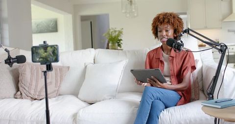Woman recording podcast at home speaking into boom microphone with tablet and smartphone