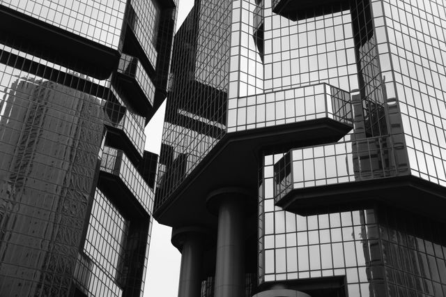 Close-up of a modern skyscraper with geometric design and glass facade in black and white. Suitable for illustrating urban development, modern architecture, and city life. Ideal for use in architectural magazines, urban planning presentations, and real estate promotions.
