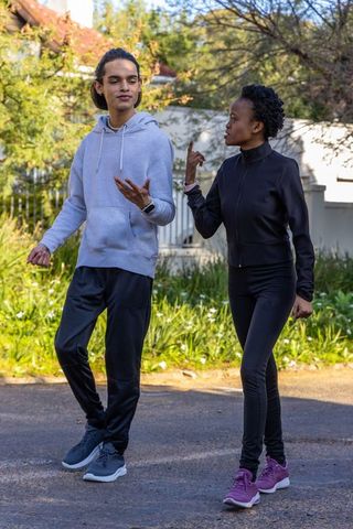 Young friends walking and comparing smartwatch fitness data while talking on suburban street