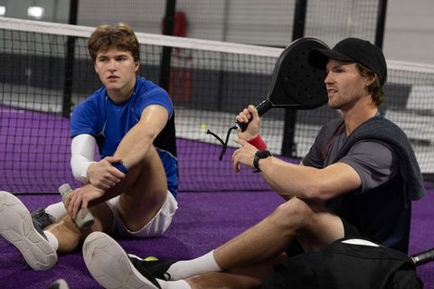 Padel duo resting on purple court after intense training session, holding paddles