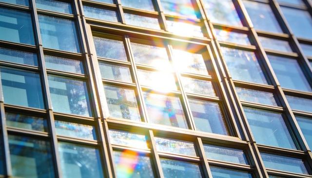 Sunlit glass facade with prism flares on modern urban building grid and rainbow reflections