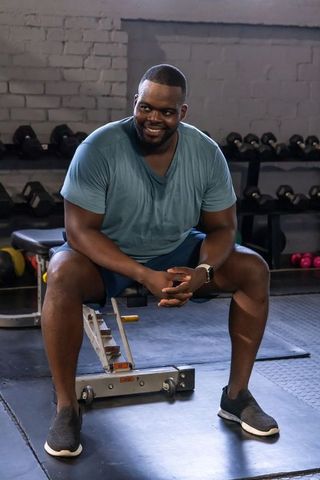 African man sitting and resting between sets on adjustable bench in gym