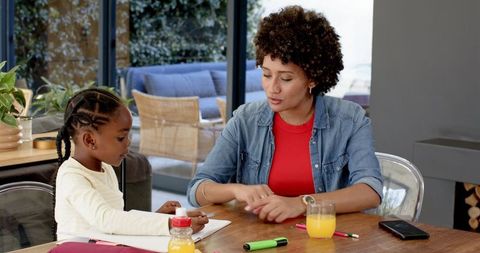 Mother Guiding Daughter with Homework at Dining Table