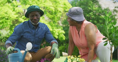 a senior african american couple enjoys gardening together on a bright, sunny day. they are tending to vibrant flowers, sharing a moment of teamwork and happiness. perfect for illustrating themes of senior lifestyle, outdoor hobbies, and maintaining an active retirement life.