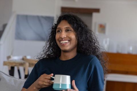 Smiling african american woman enjoying coffee on sofa in cozy modern living room