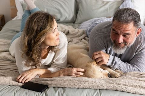 Mature couple lounging on bed with sleeping golden retriever puppy, cozy morning moment