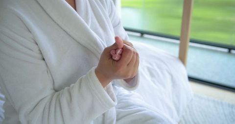 African american woman clasping hands wearing white bathrobe showing ring and pink nails