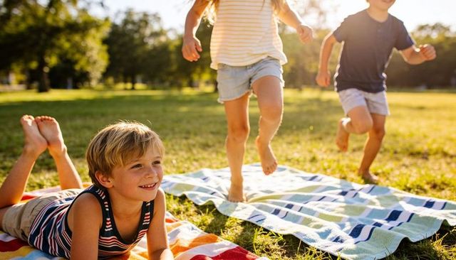 Smiling boy and friends playing on striped blankets in sunlit park at golden hour