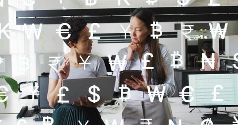 Businesswomen collaborating on financial data with laptop and tablet in modern open office
