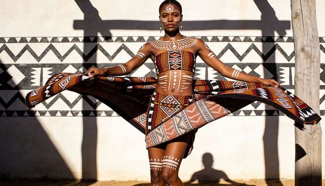Spinning in geometric printed wrap with white body paint, sunlit courtyard fashion pose