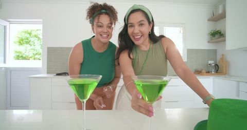 Multicultural friends toasting with vibrant green cocktails in bright modern kitchen