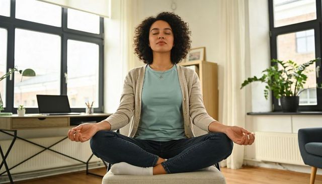 Woman meditating in sunlit home office taking mindful break during remote workday