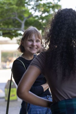 Friends sharing laughs on tree-lined urban plaza during casual outdoor conversation