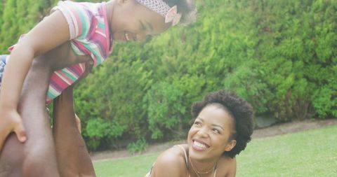Joyful Family Playing with Daughter Outdoors in Lush Garden