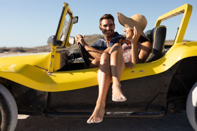 This image shows a happy couple enjoying a sunny day at the beach, sitting in a yellow buggy. They are smiling and talking, with the beach and blue sky in the background. Ideal for use in travel promotions, summer holiday advertisements, and lifestyle blogs.