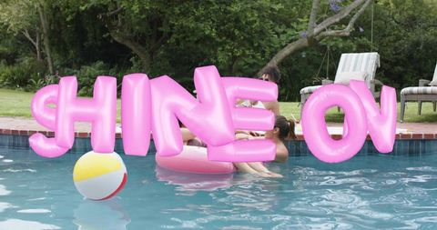 Giant pink inflatable letters spelling shine on floating over backyard pool party
