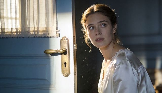 Young woman in vintage satin slip peeking through sunlit door with brass handle and dust motes